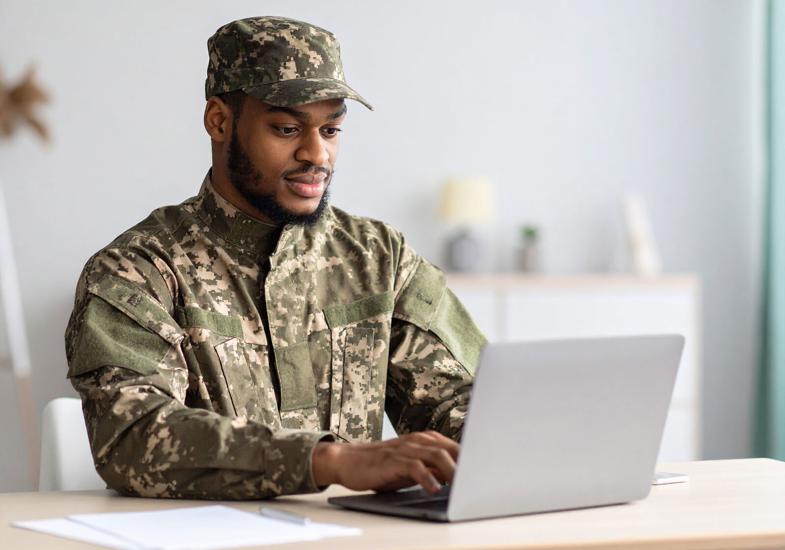 man-on-military-uniform-searching-the-web-on-a-laptop,-seating-on-a-table-at-home man-on-military-uniform-searching-the-web-on-a-laptop,-seating-on-a-table-at-home
