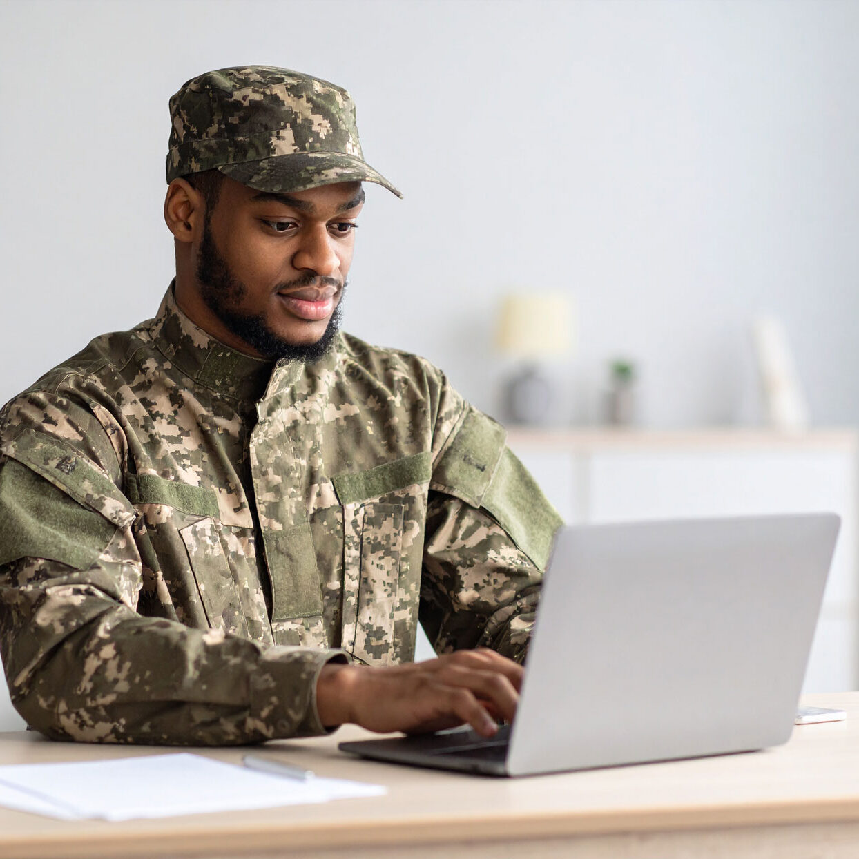 man-on-military-uniform-searching-the-web-on-a-laptop,-seating-on-a-table-at-home